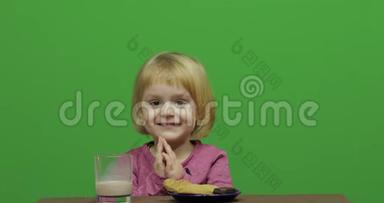 女孩坐在桌子旁<strong>吃</strong>巧克力、<strong>饼干</strong>和饮料可可。 快乐的三岁女孩。 可爱的女孩<strong>微笑</strong>